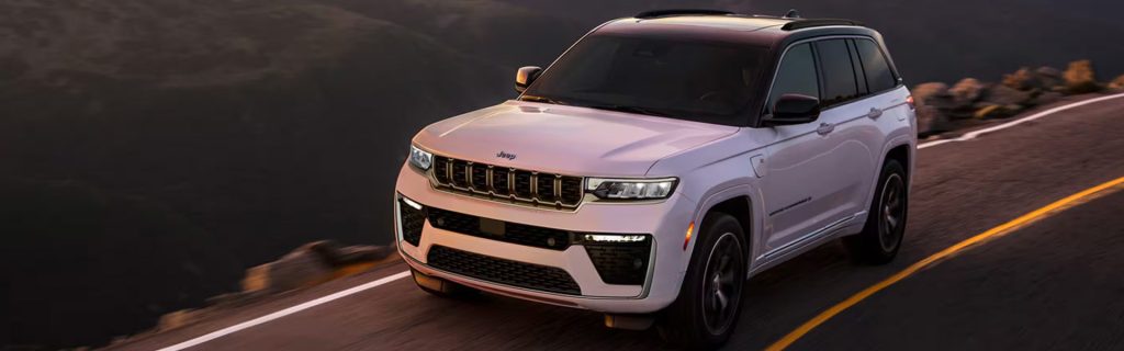 2026 Jeep Grand Cherokee driving on a scenic highway at sunset