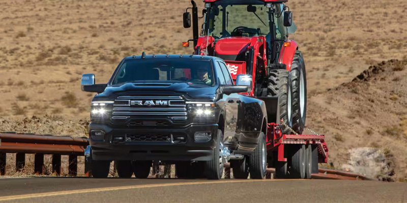2026 RAM 3500 towing a tractor, showcasing its impressive towing capacity and heavy-duty performance on the road.