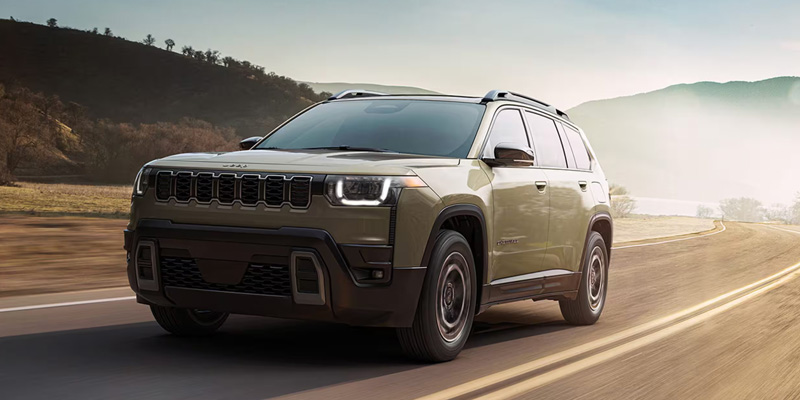 2026 Jeep Grand Cherokee driving through a scenic road, showcasing its rugged design and off-road capability.