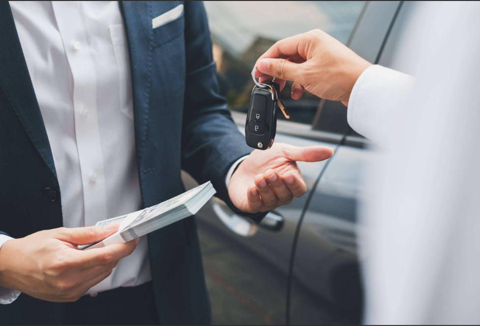 Person handing over car keys and paperwork during a vehicle purchase transaction.