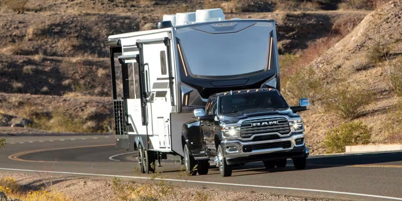 Black Ram pickup truck towing a large travel trailer on a winding mountain road.